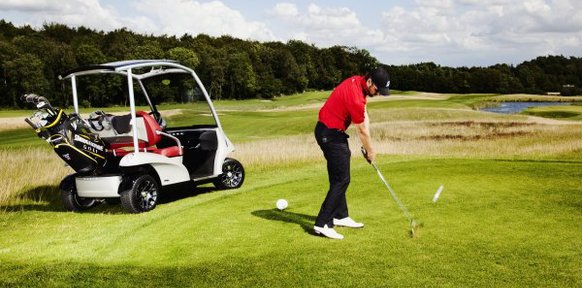 На поле гольфкар и гольфист бьет по мячу для гольфа клюшкой